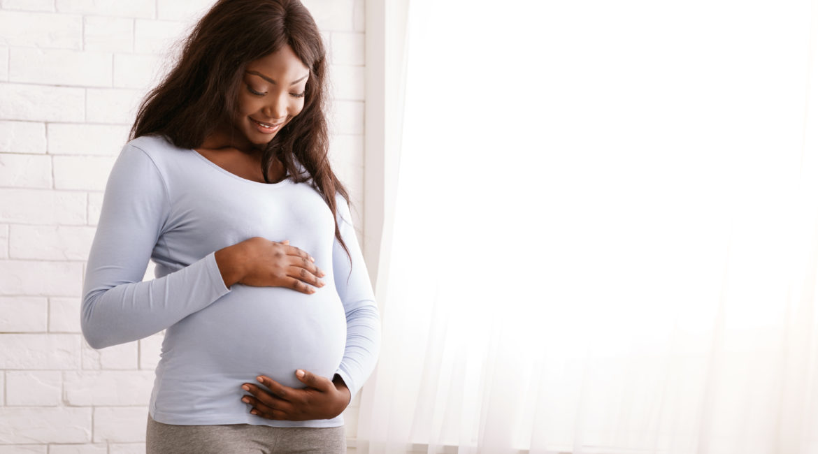 A pregnant African American woman smiling and holding her stomach