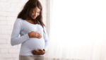 A pregnant African American woman smiling and holding her stomach