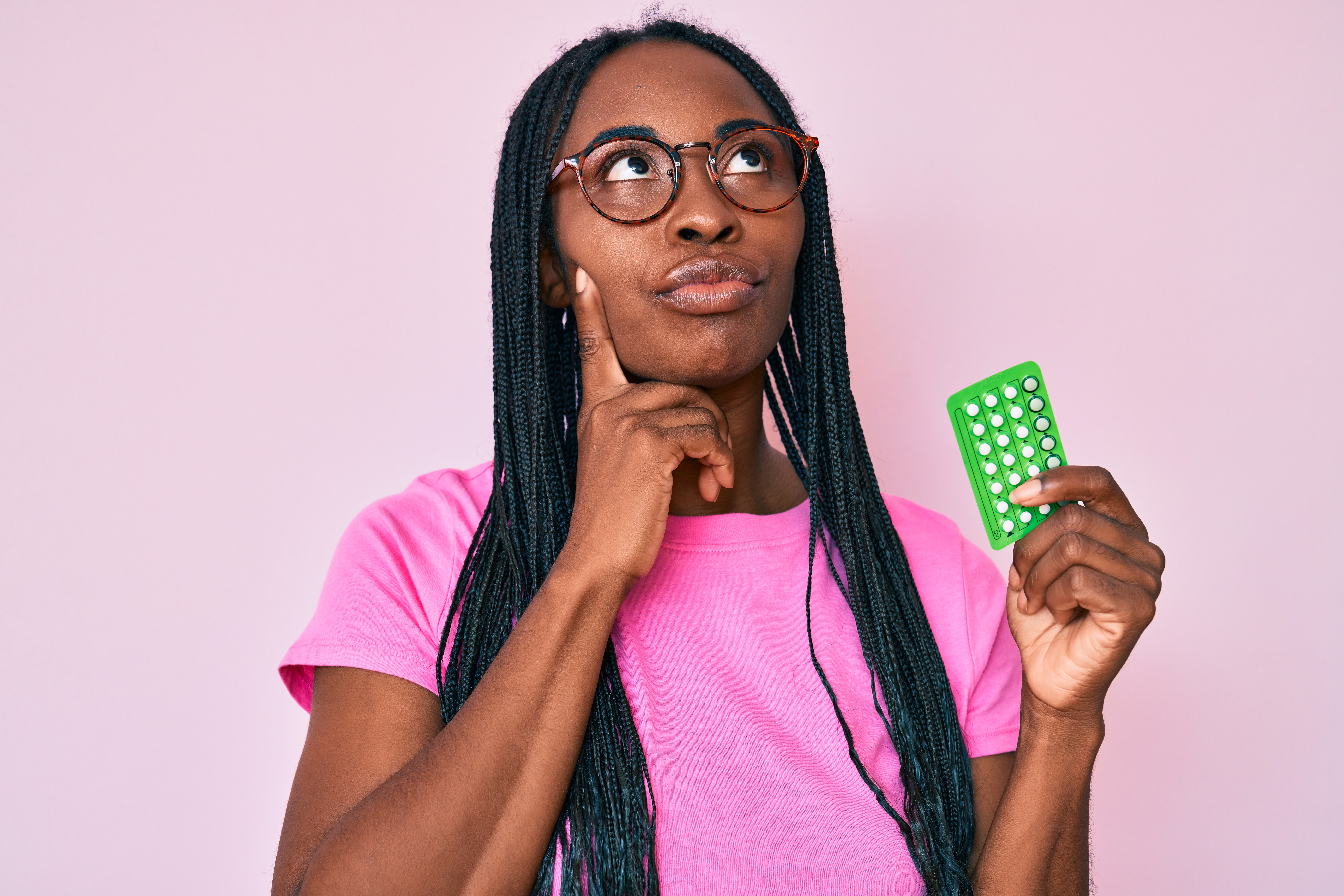 A young African American woman holding birth control pills while thinking