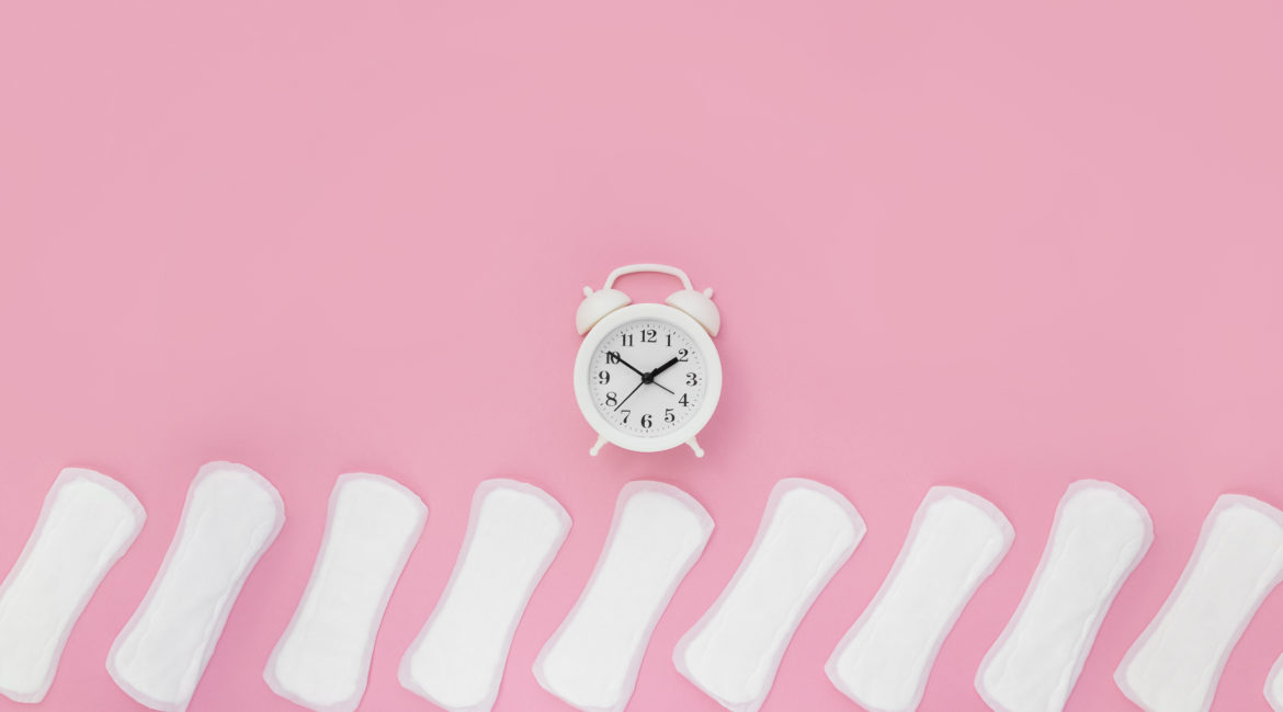 Menstrual pads and a white alarm clock sit on a pink background