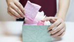 A woman reaches into a box to pull out a menstrual pad wrapped in pink plastic.